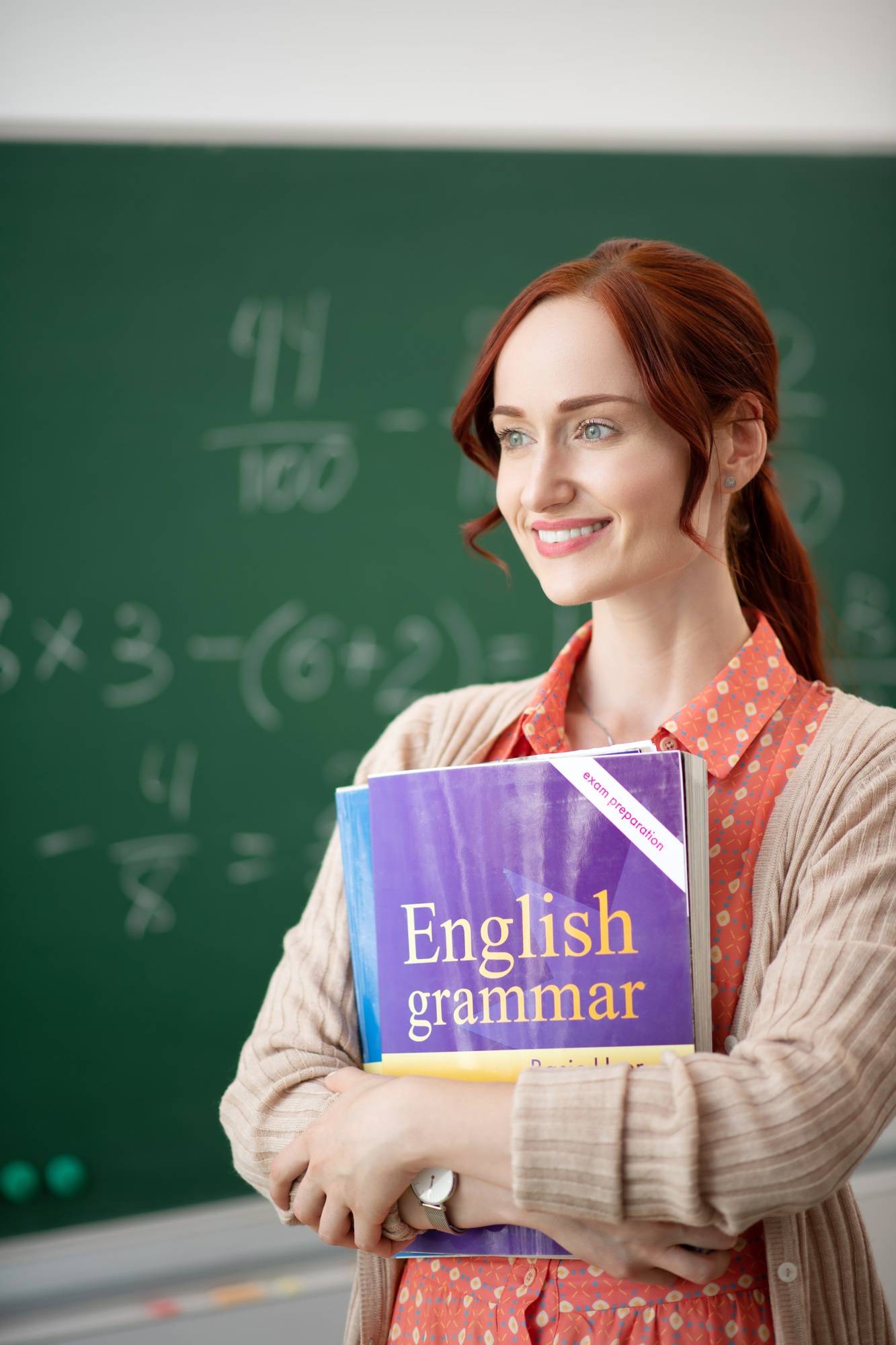 Beaming teacher holding books standing in classroom